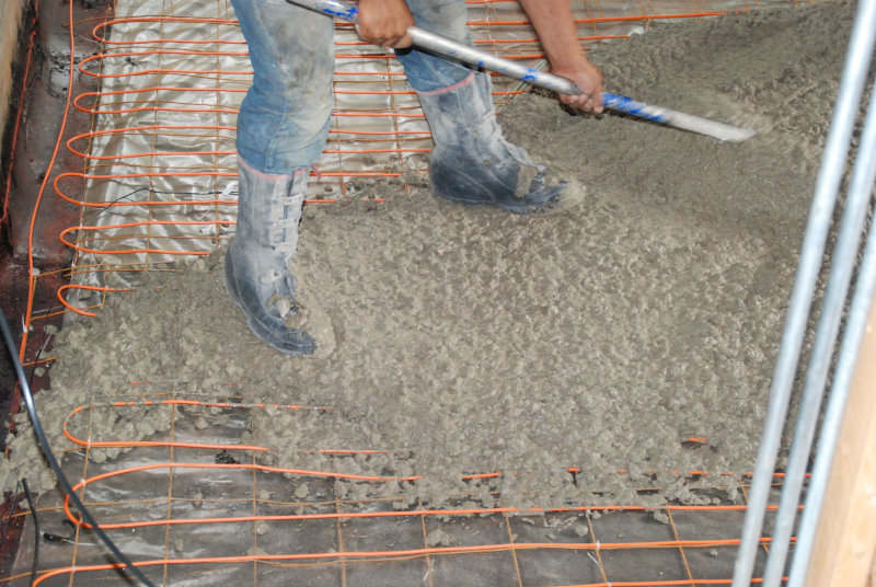 photo of man spreading concrete mix onto floor heating elements